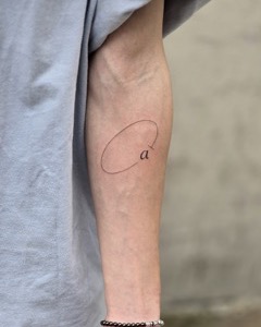 Fine-line lowercase a with an open oval tattooed on the inner forearm in Seoul