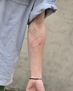 Wide view of a minimalist lowercase a and open oval tattoo on the inner forearm