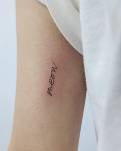 Fine-line "meow" lettering tattoo on the upper arm, Seoul